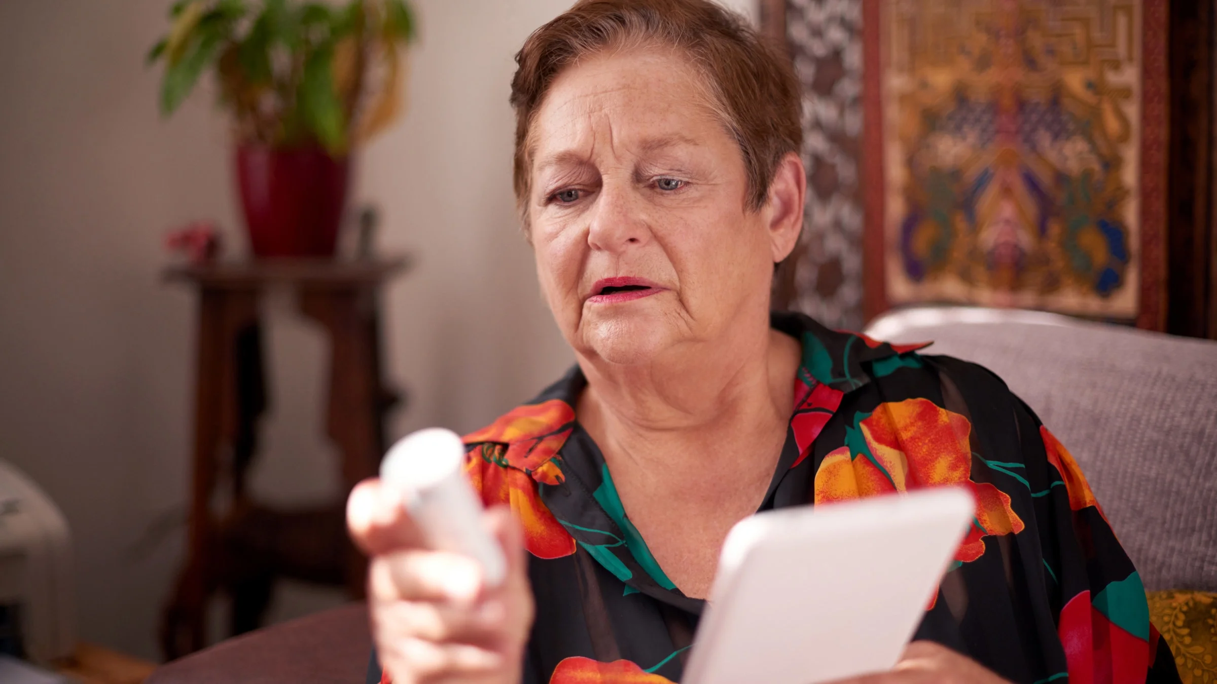 A person holding a pill bottle and a tablet. 