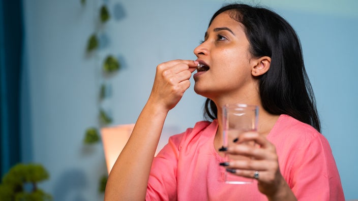 A woman prepares to take a tablet with a glass of water.