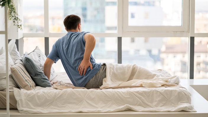 A person with back pain trying to get up from their bed in the morning.