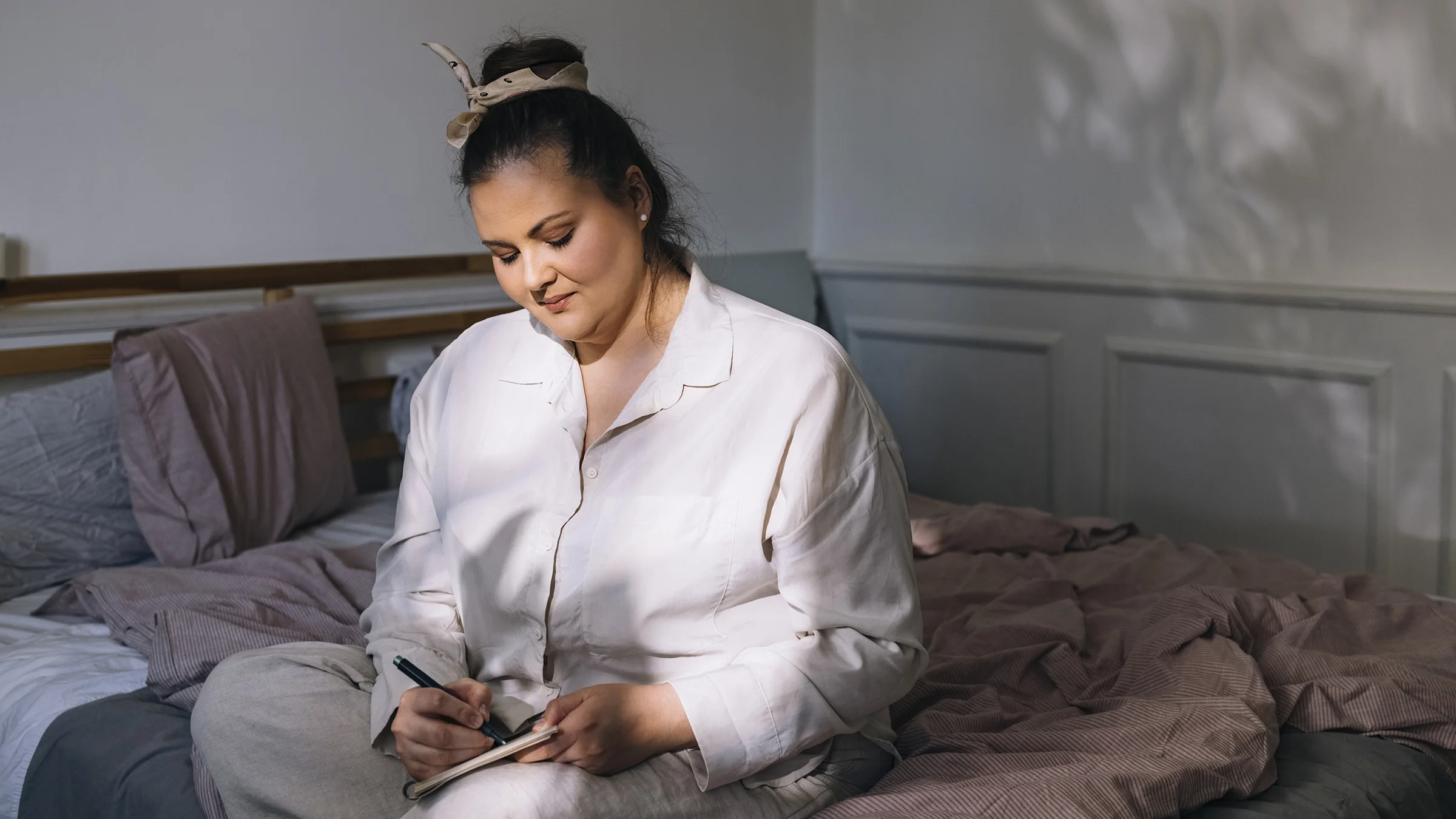 A woman in her pajamas writes a to-do list before bedtime.