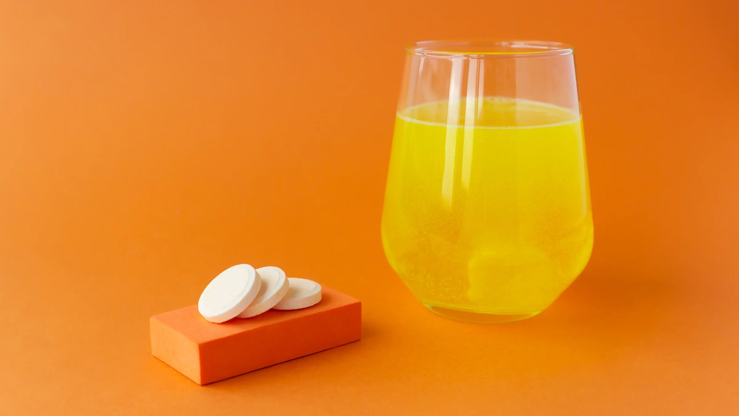 Emergen C tablets and a glass with a tablet fizzing on an orange background.
