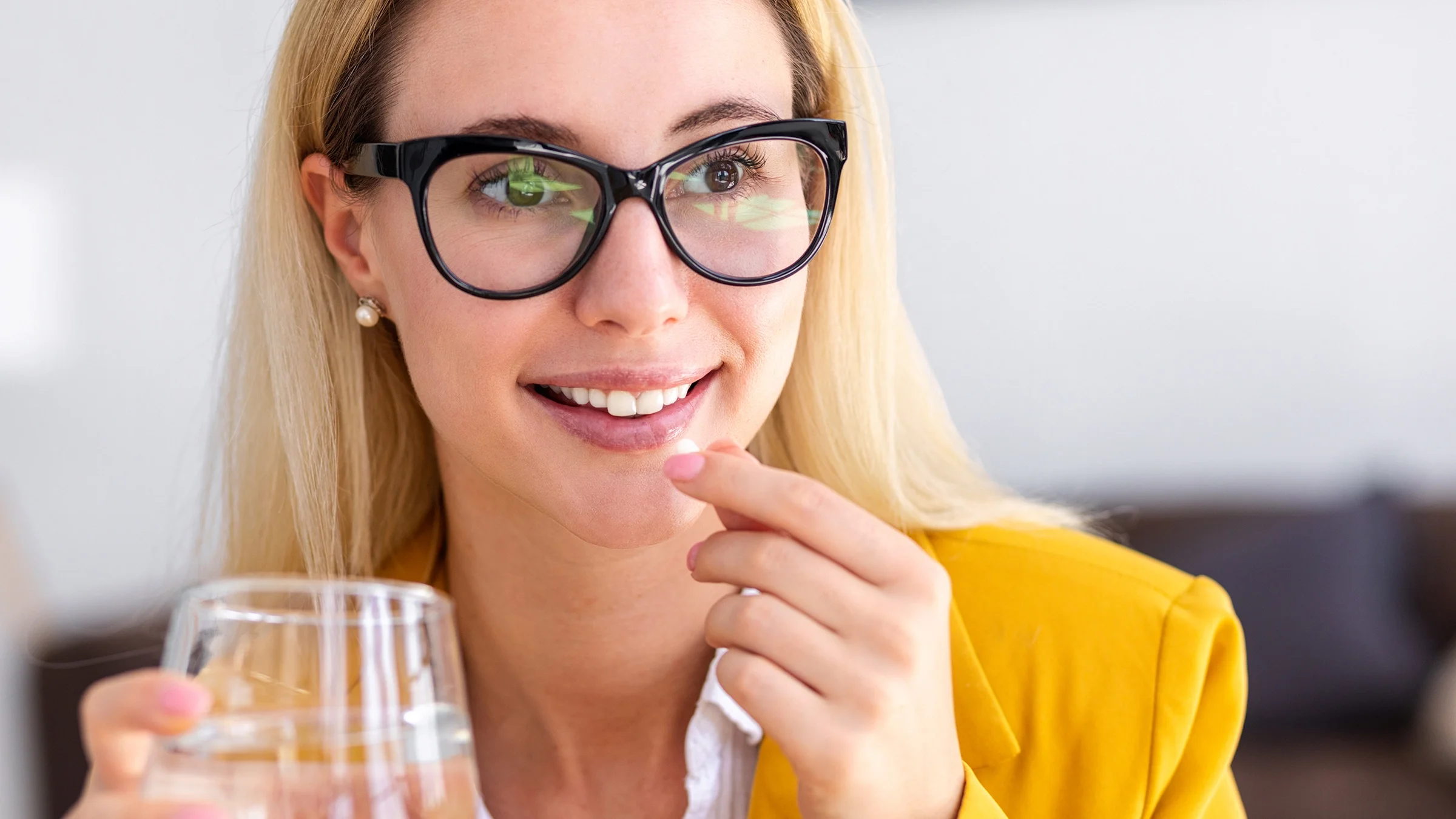 Young woman with glasses taking a white pill with a glass of water.