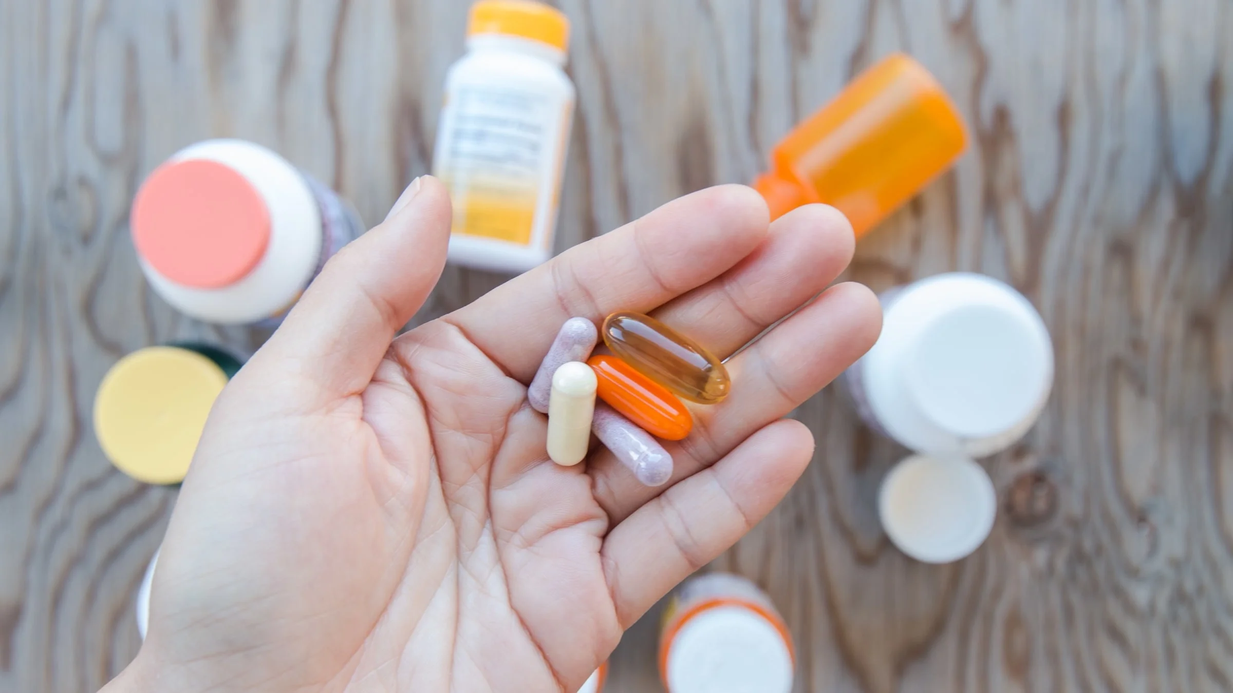 A handful of colorful supplements. There are pill bottles in the background.
