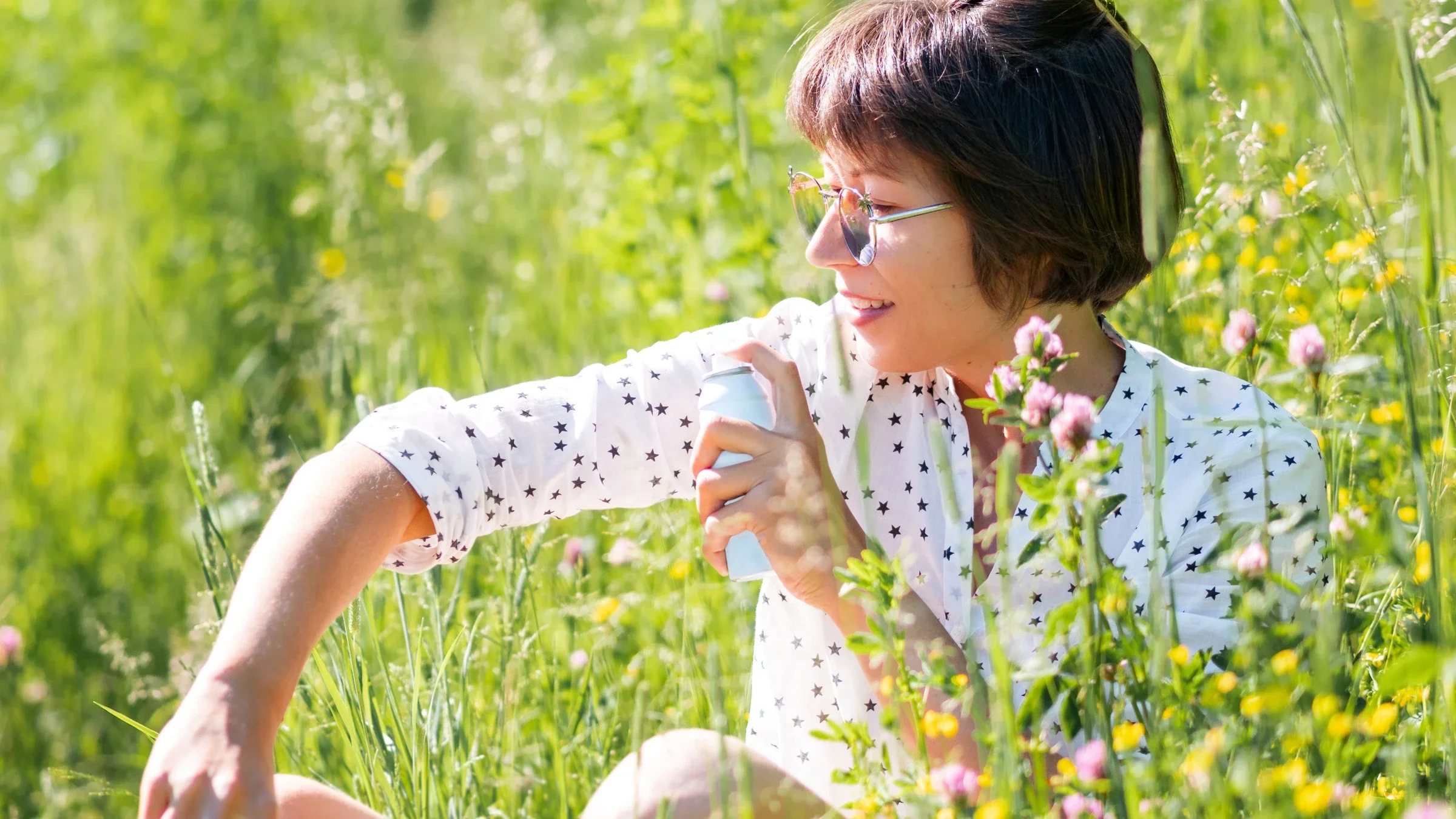 A person spraying bug repellant in a flower field.