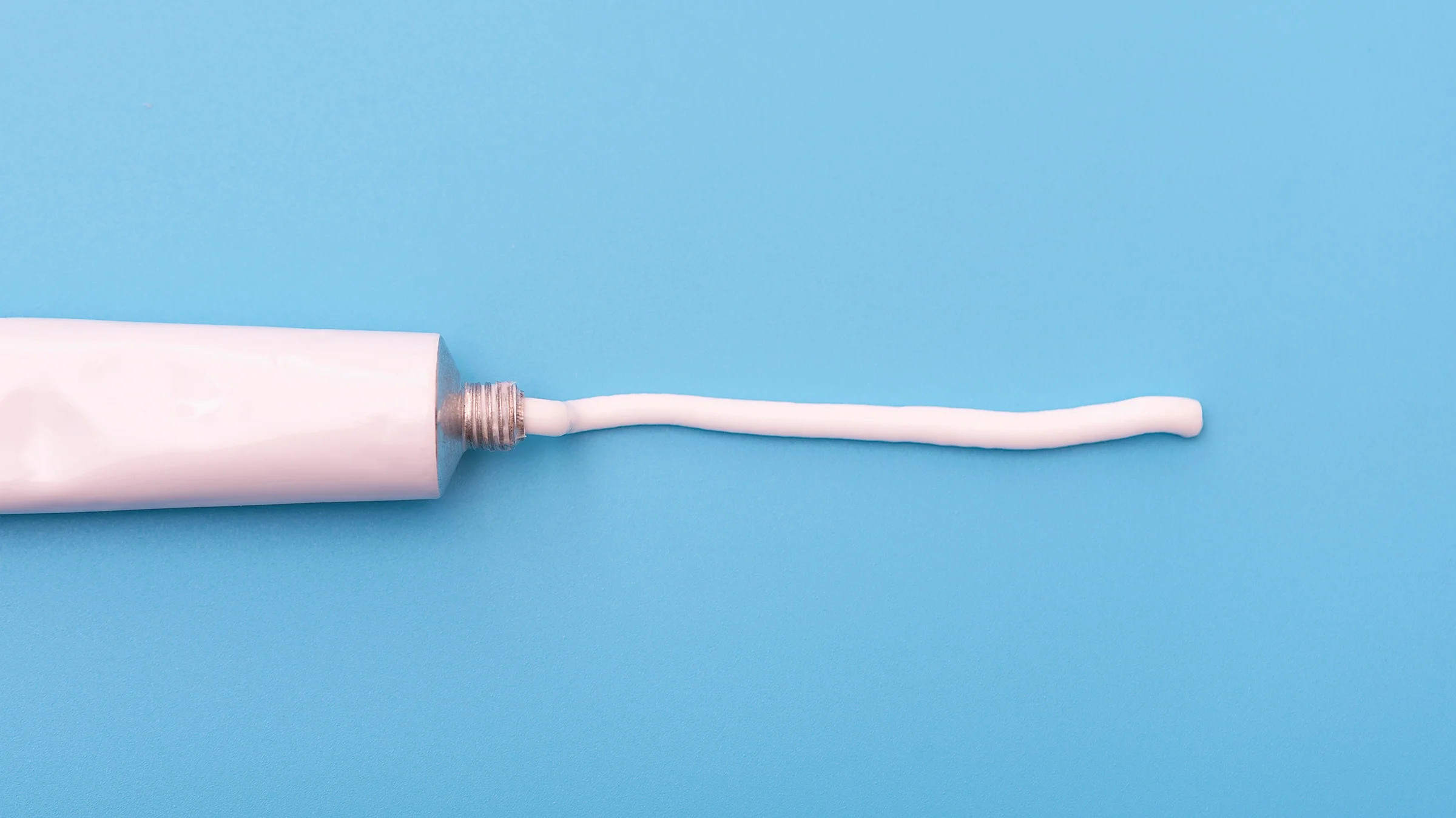 White ointment tube with white cream line on blue background.