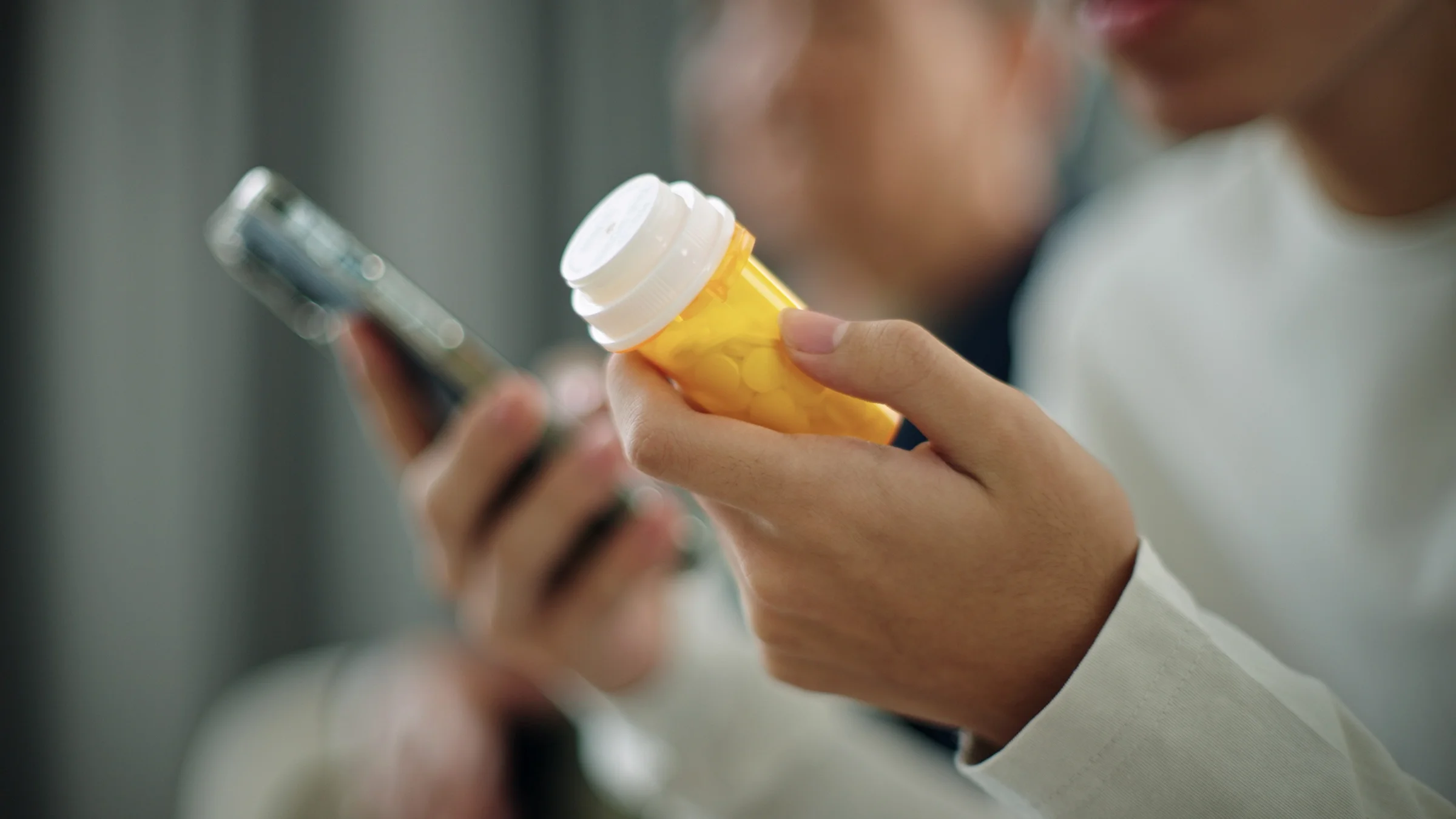 A person is holding a prescription pill bottle, looking up the medication on a smart phone.