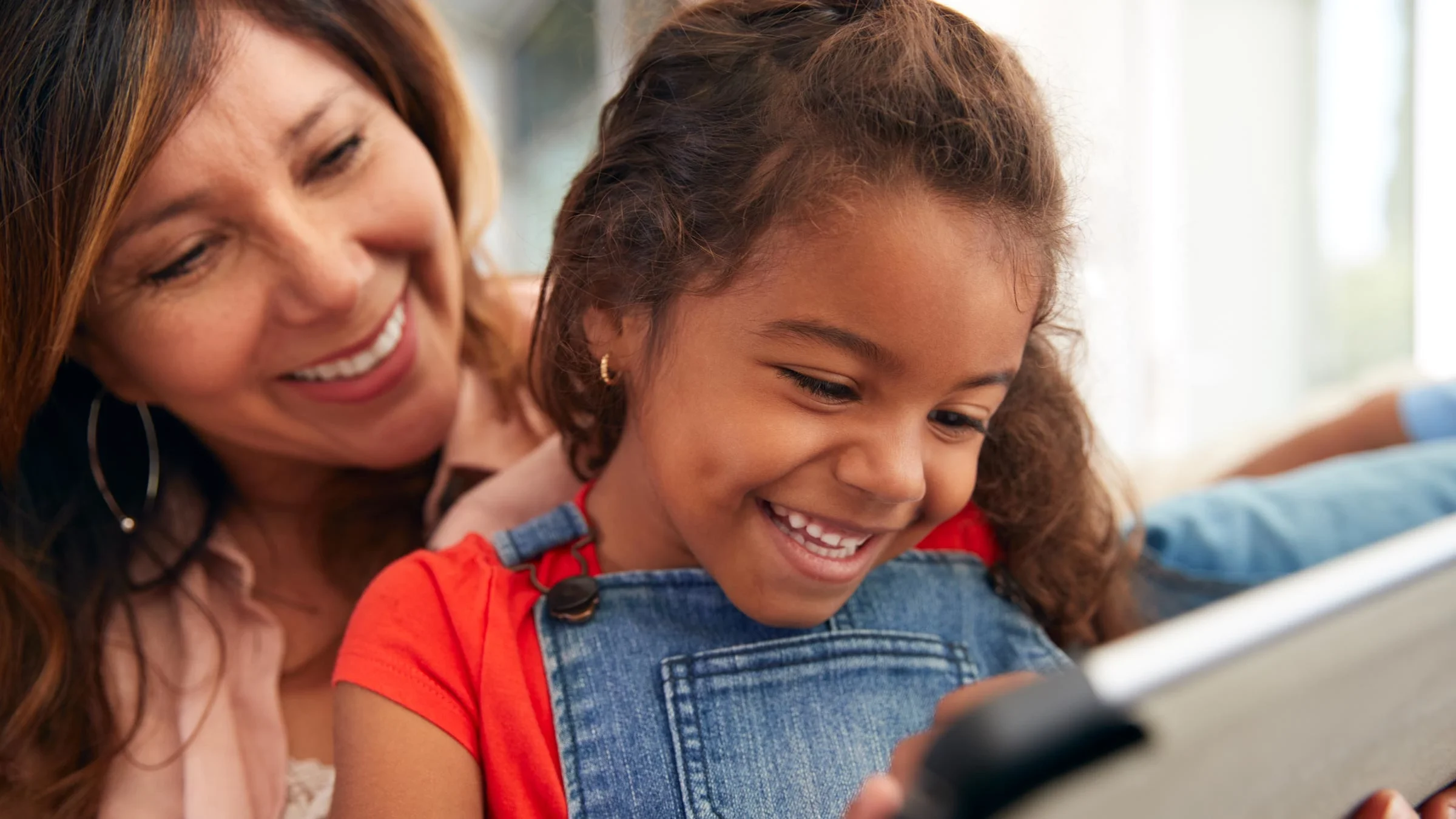 A woman and a little girl smile while using a computer tablet together.