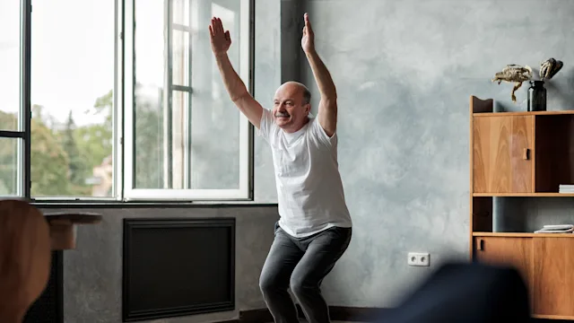 Movement exercise: senior man doing yoga chair pose 1177407582