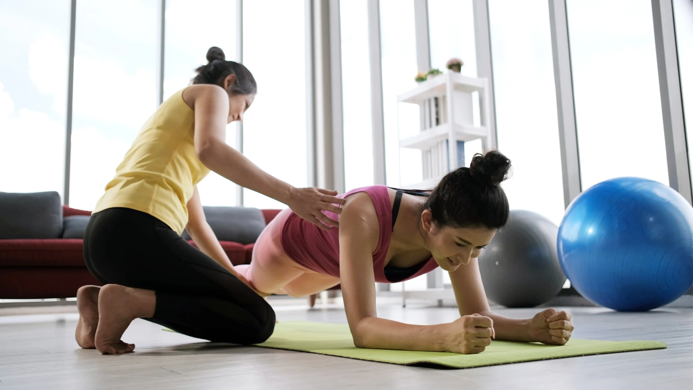 Woman getting help with plank exercise from workout instructor.