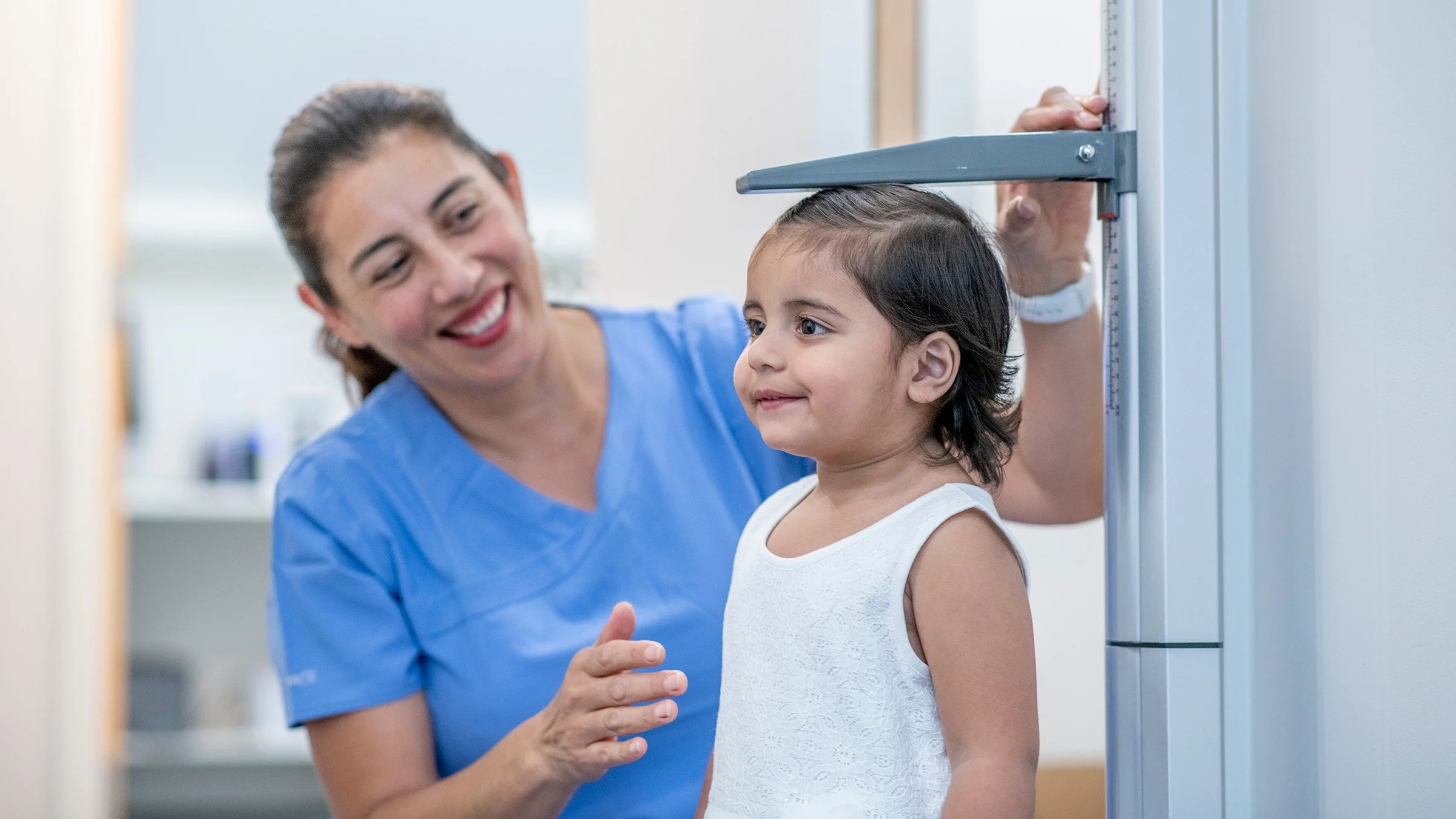 A nurse with their hair pulled back while measuring a small child’s height at the doctor's office.