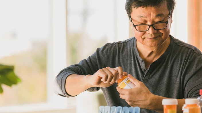 Senior man opening a prescription bottle. He has a pill organizer in front of him.