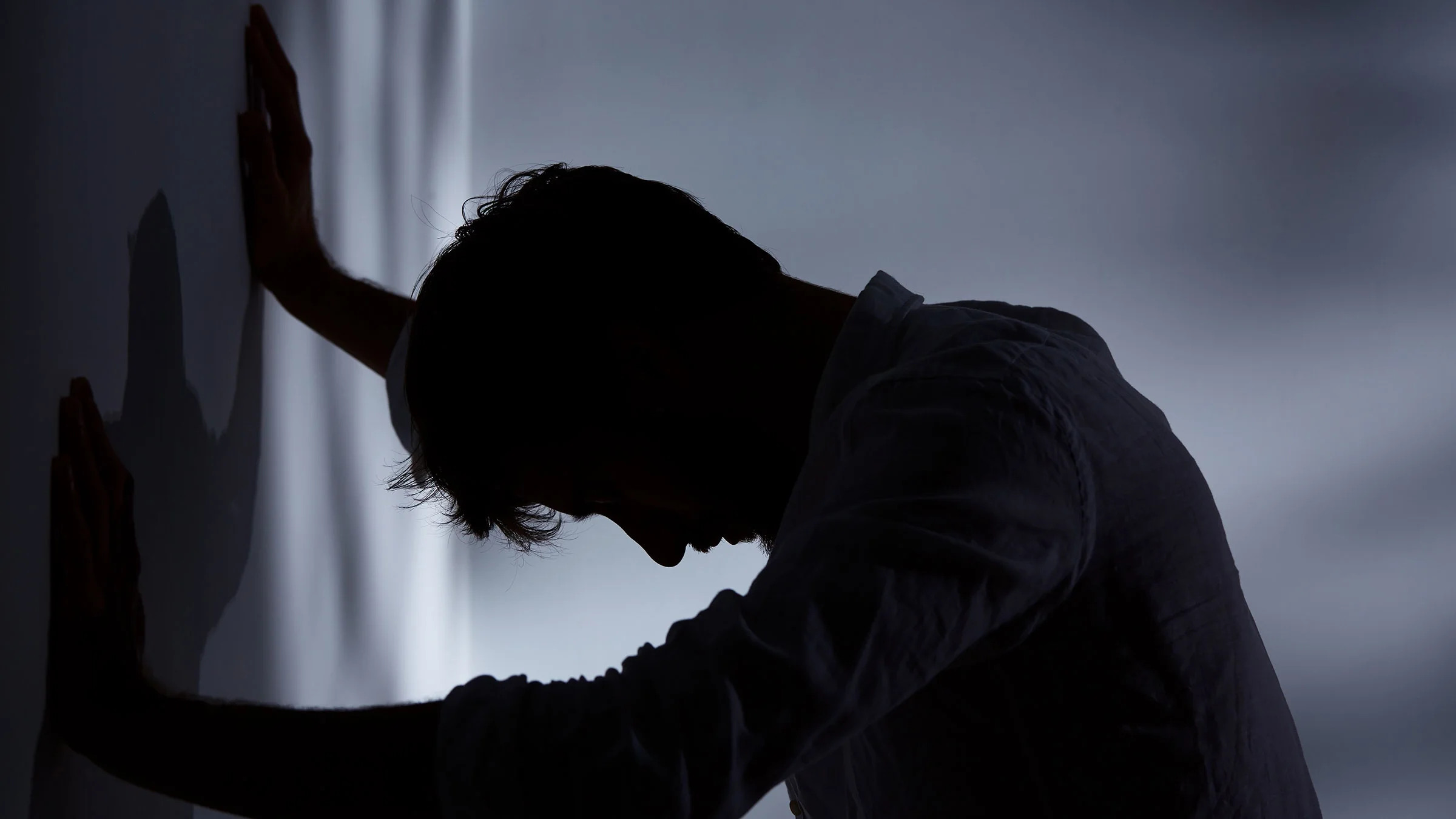 Silhouette of man leaning up against wall in a dark room