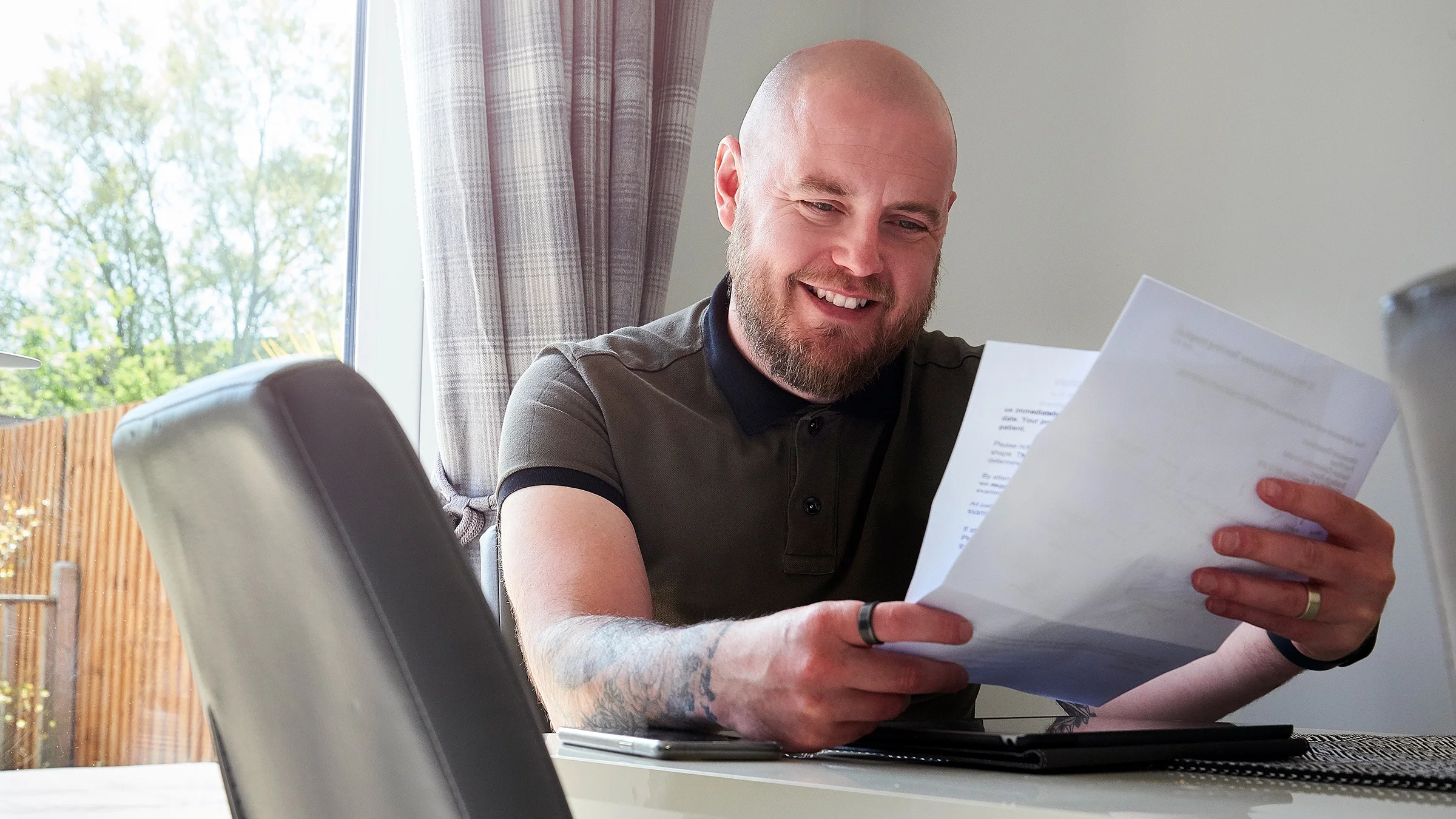 A man is smiling while reading a letter at home.
