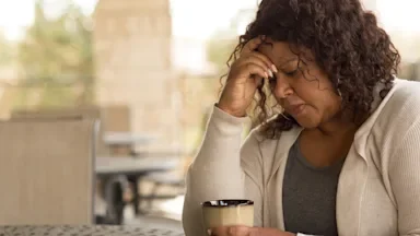 Woman sitting at a patio table with her morning coffee. She has her hand on her forehead in distress.
digitalskillet/iStock via Getty Images
