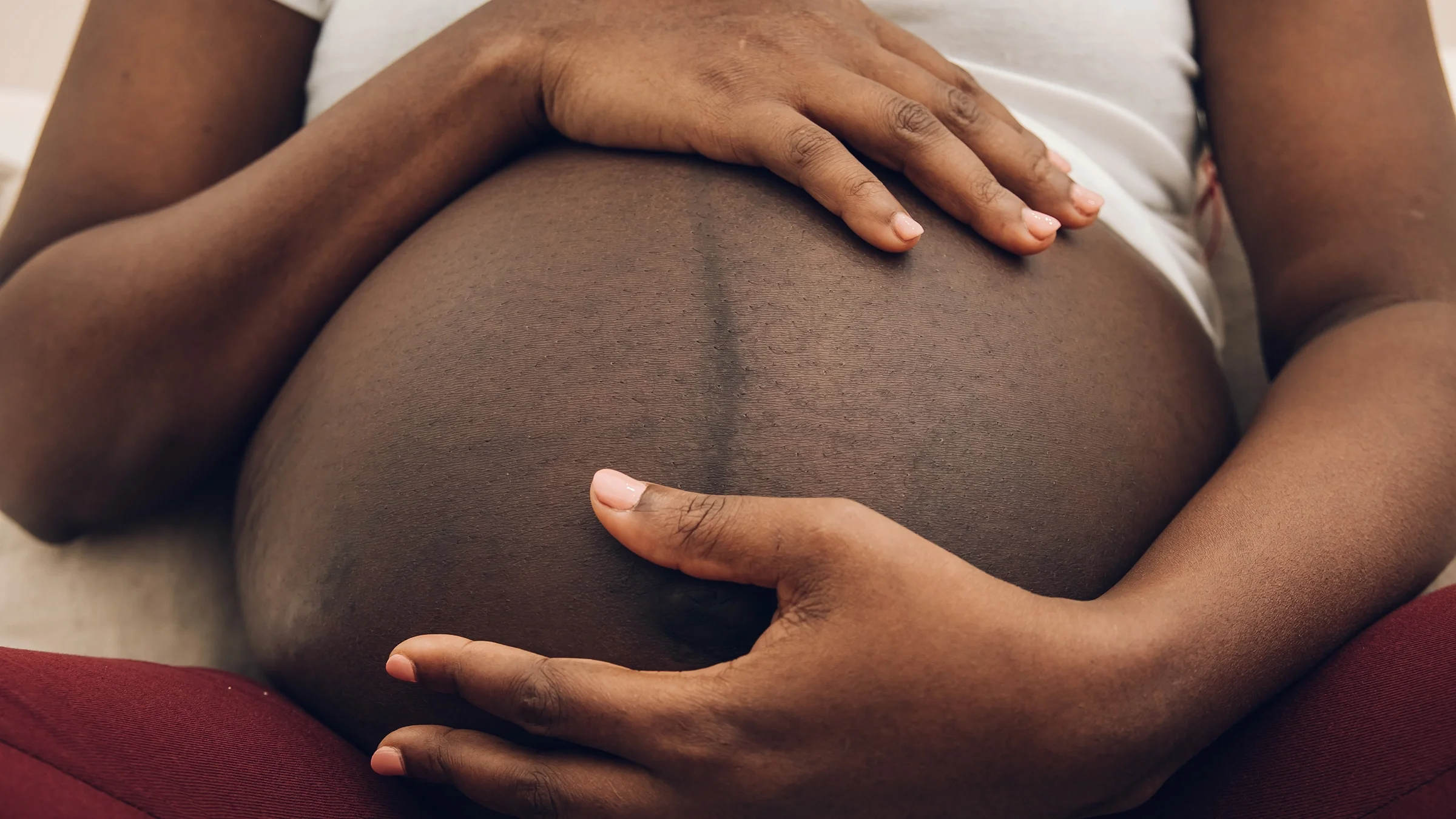 Cropped shot of a Black pregnant person holding and embracing their pregnant belly.