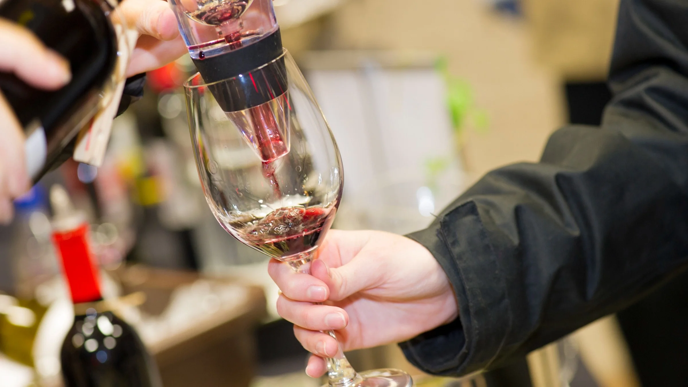 Close-up cropped shot of a person serving a glass of red wine. They are pouring it through an aerator first.
