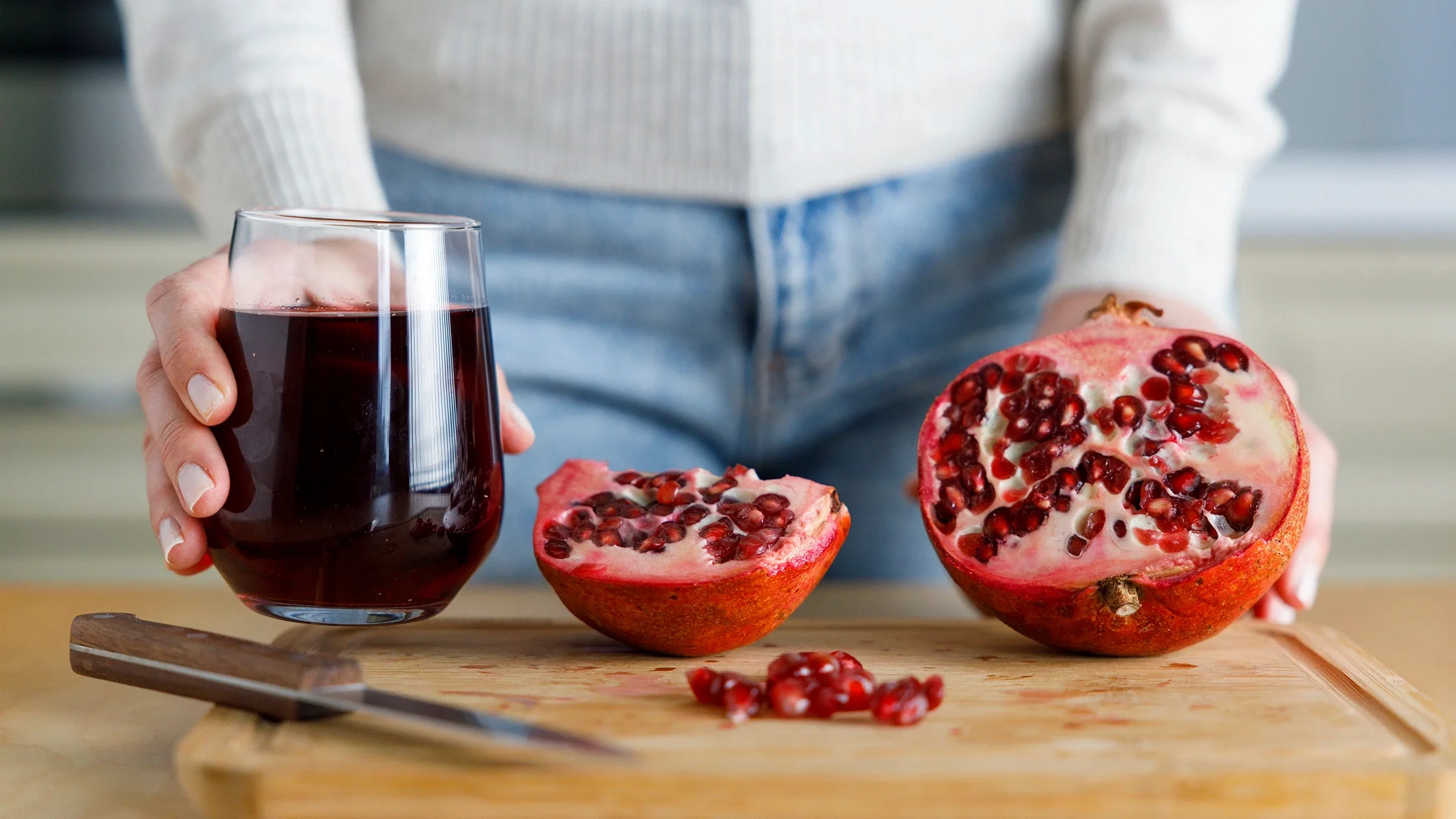 Close-up hand holding a glass of pomegranate juice with fresh pomegranate.