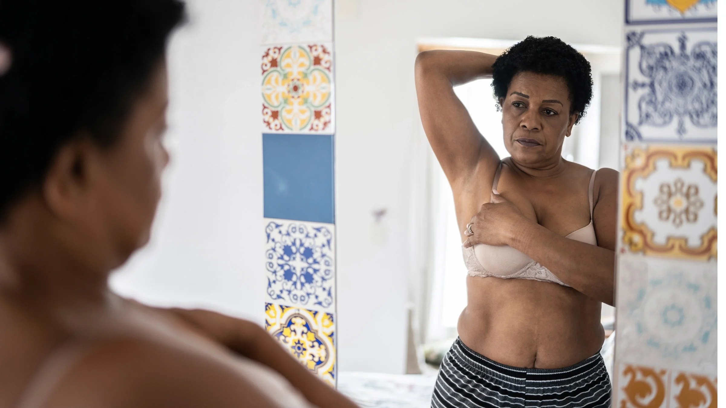A person conducting a self breast exam in a colorful mirror. About half of all women have dense breasts, which means their breasts have less fat than fibrous tissue and glands.