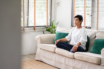 Senior woman meditating on her couch sitting cross-legged.