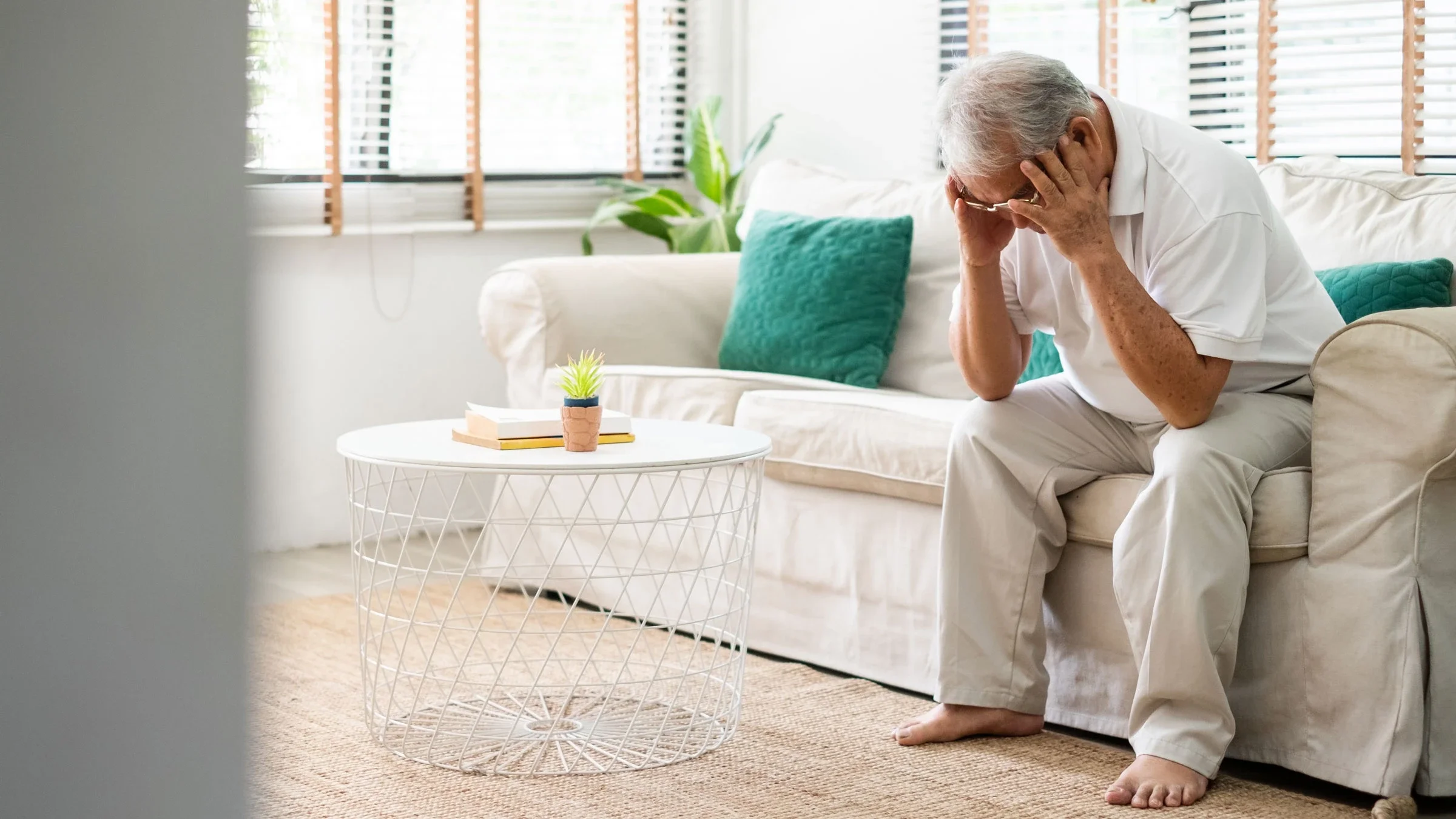 Senior man with headache sitting alone on sofa at home.
