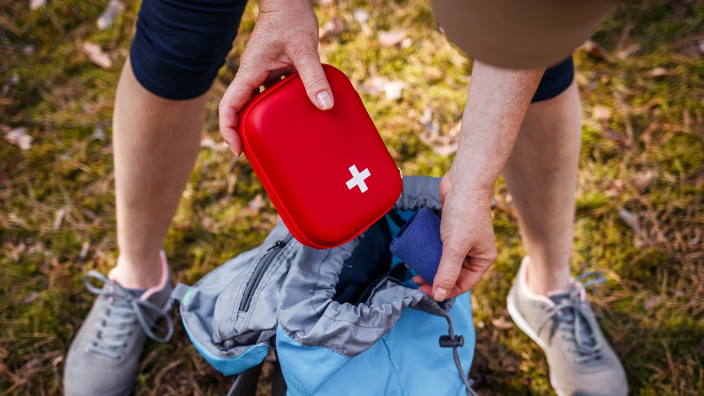An adult is taking out a first-aid kit from their backpack.