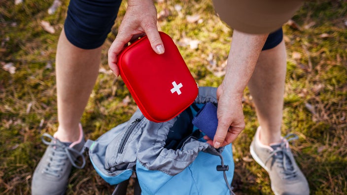 An adult is taking out a first-aid kit from their backpack.