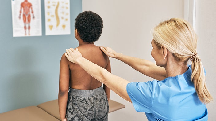 Nurse performing a scoliosis check on a child in the exam room.