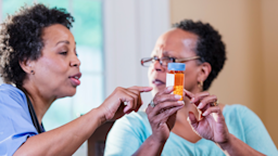 A caregiver explaining a pill bottle to a patient.
kali9/E+ via Getty Images