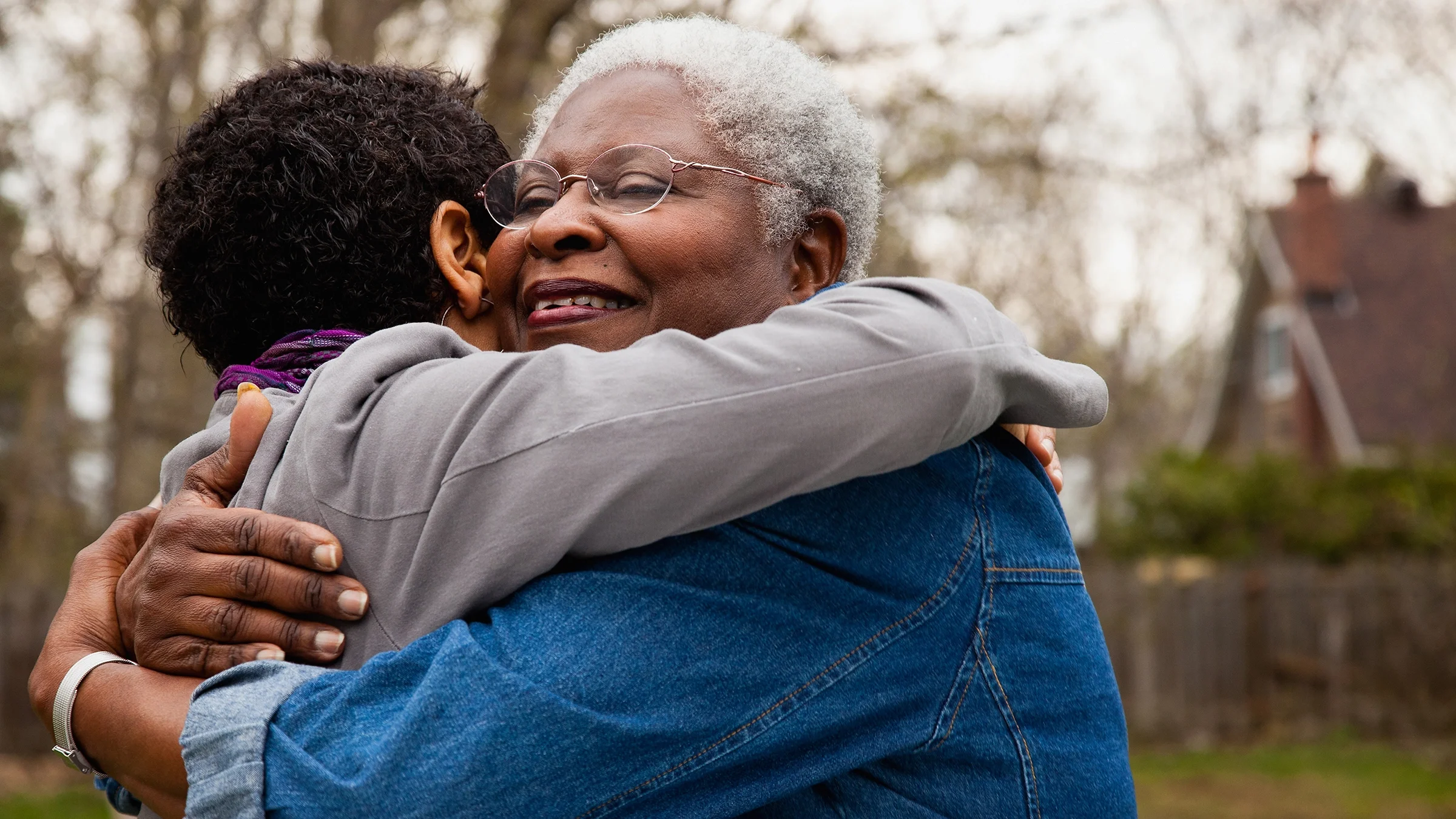 Senior woman hugging her daughter outside on a cloudy fall day.