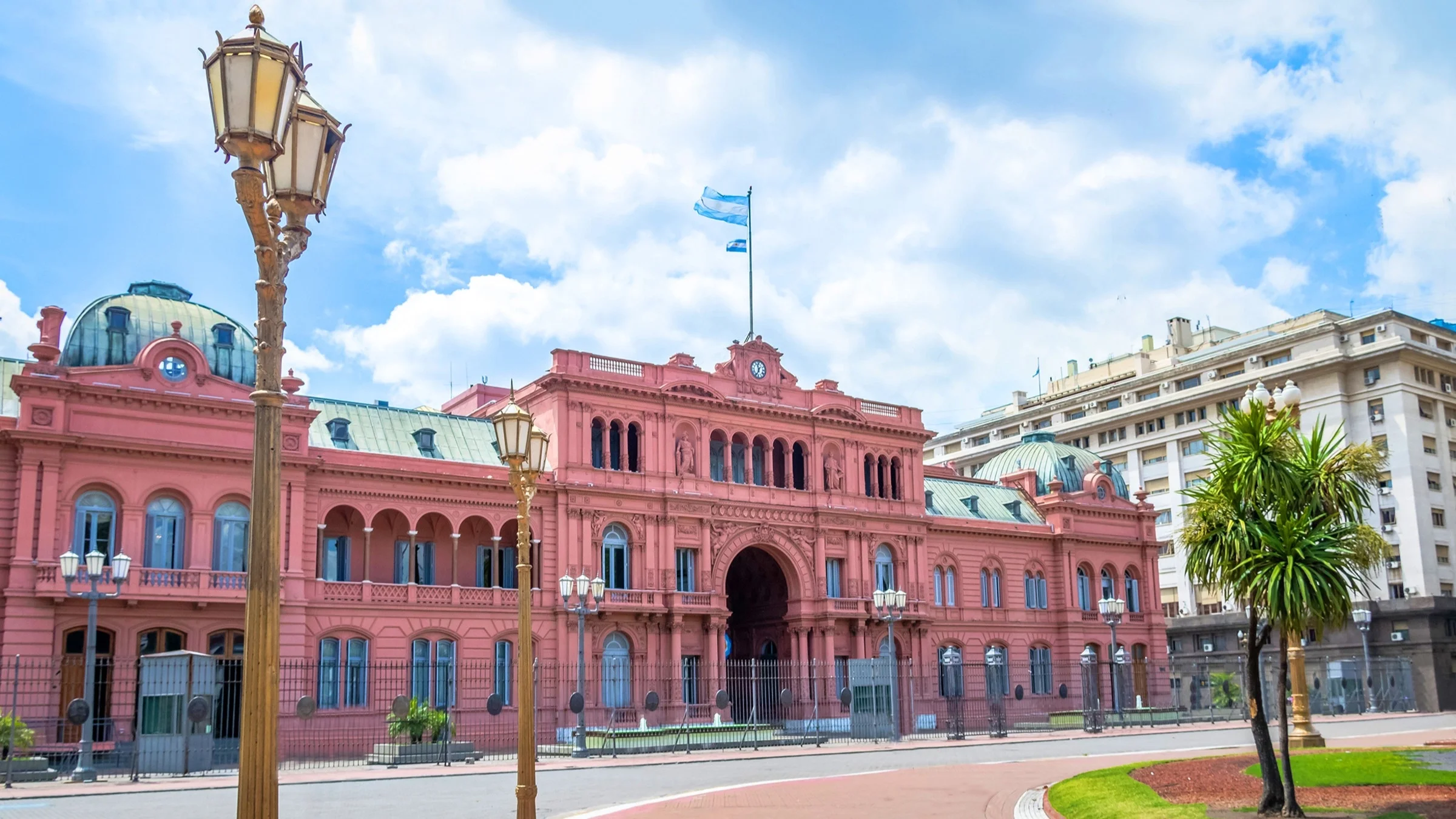 The pink presidential building in Buenos Aires that is flying the Argentinian flag above on a clear blue sky day.