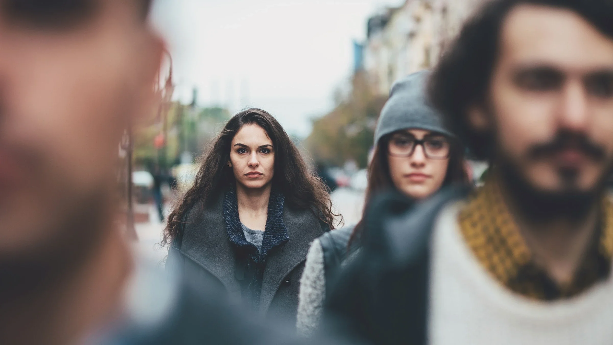 Group of young people standing in a staggered group. The focus in on a woman in the middle with long brown wavy hair.