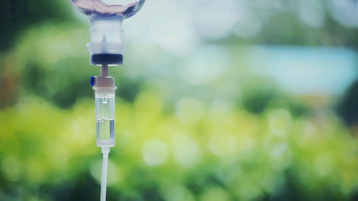 Close up of an IV drip with a blurry greenery background.