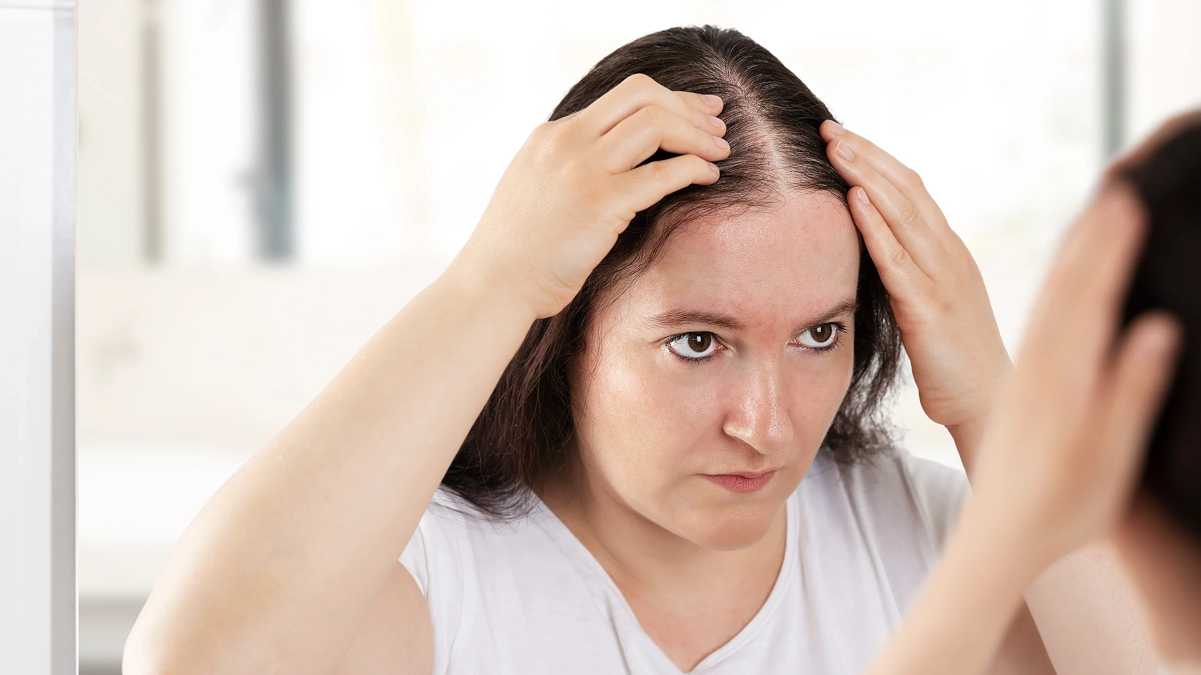 Woman examining hair loss in mirror