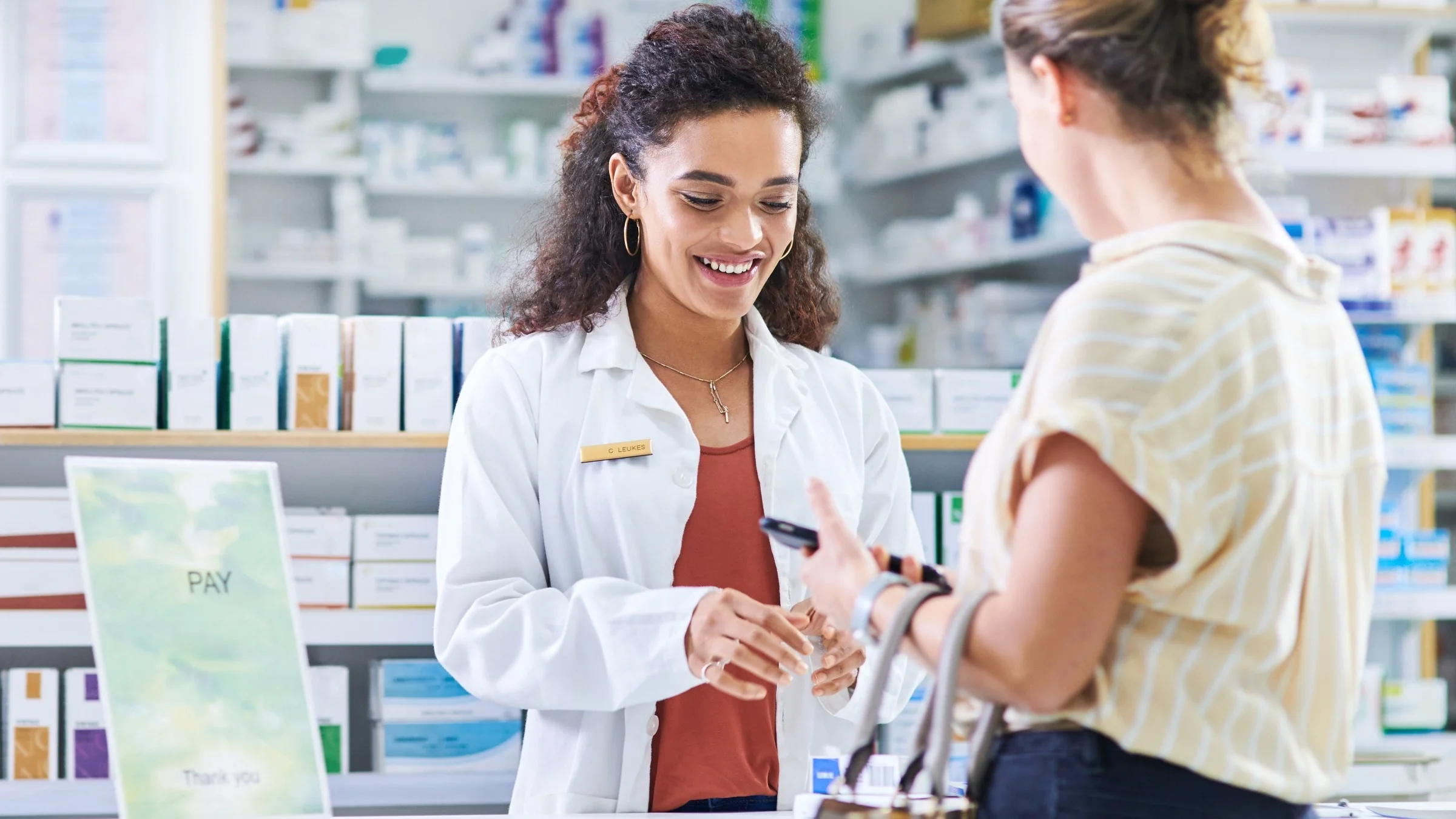 Young pharmacist assists a customer with payment at the pharmacy desk in a drugstore.