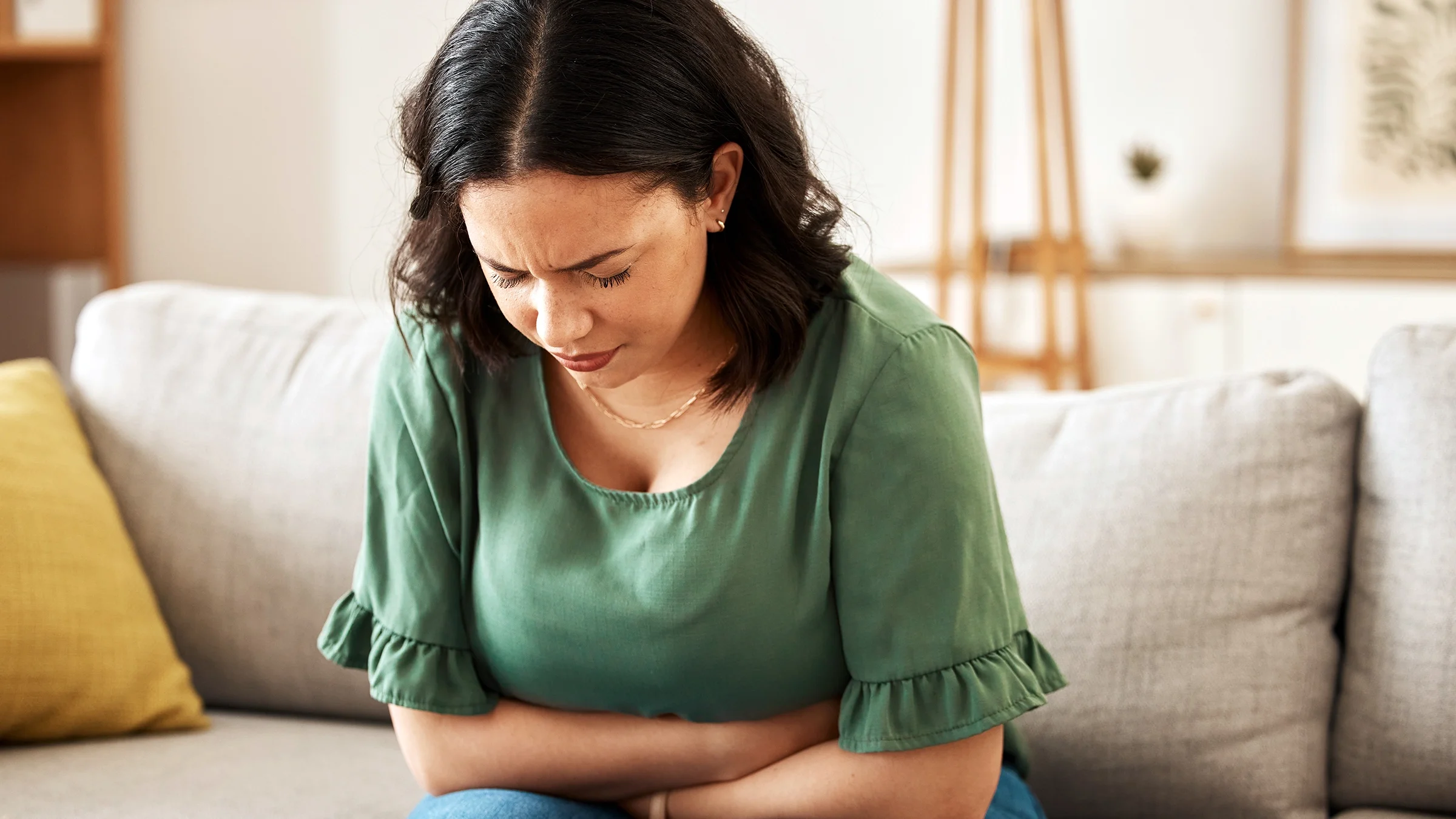 Woman experiencing bloating while sitting on a couch