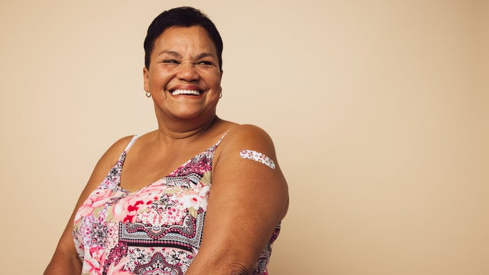 Studio portrait of an older woman smiling and showing off her band-aid from her vaccine shot.