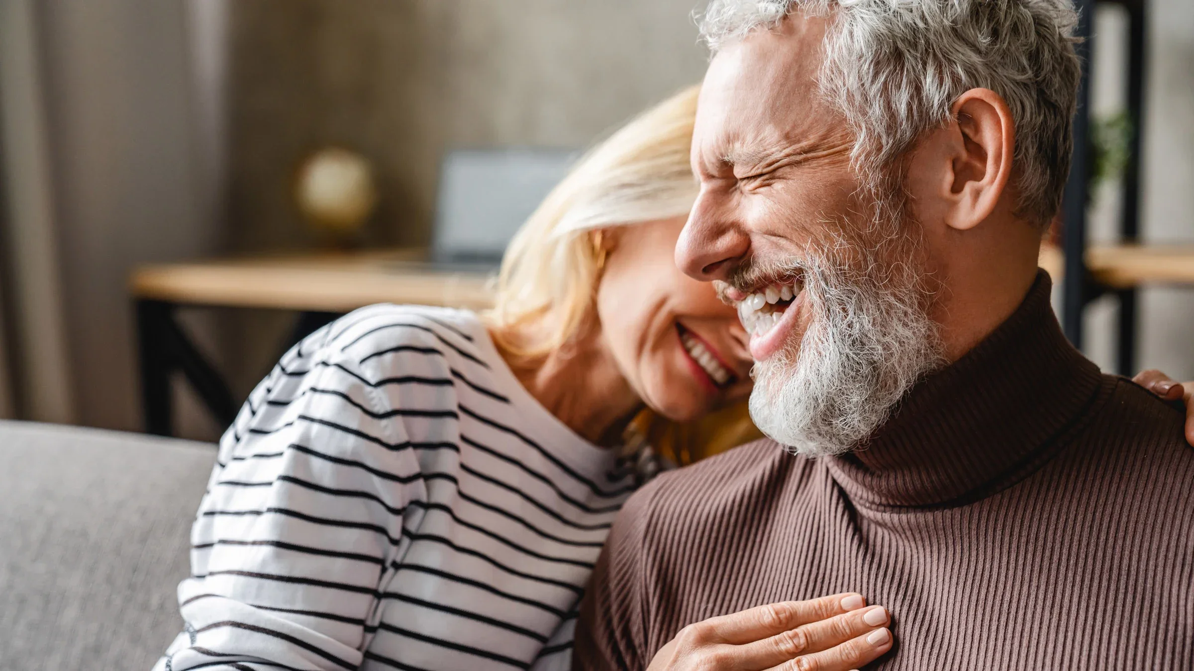 Senior couple smiling and laughing cuddling on a couch.
Inside Creative House/iStock via Getty Images