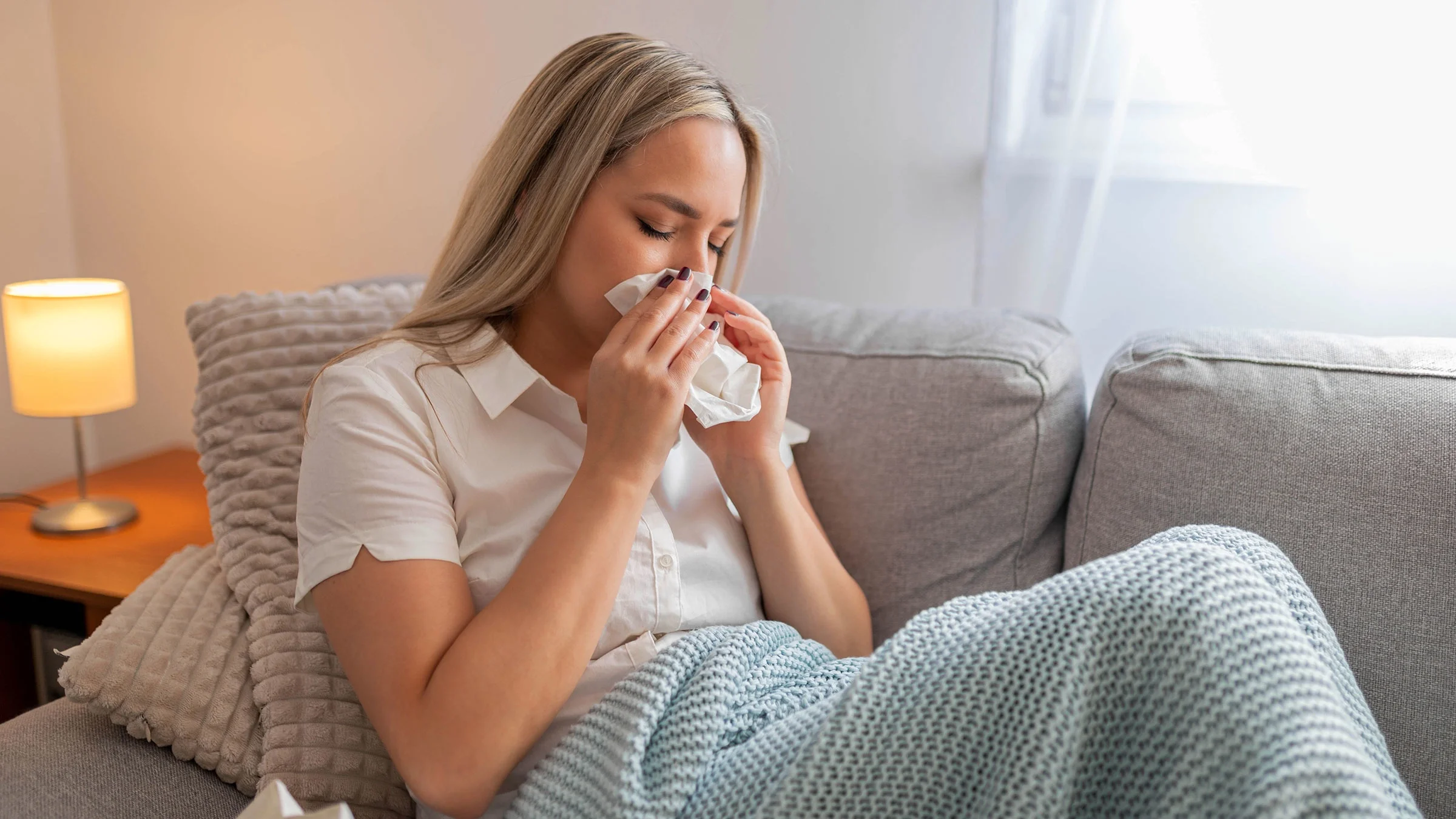 A sick woman sits under a blanket.