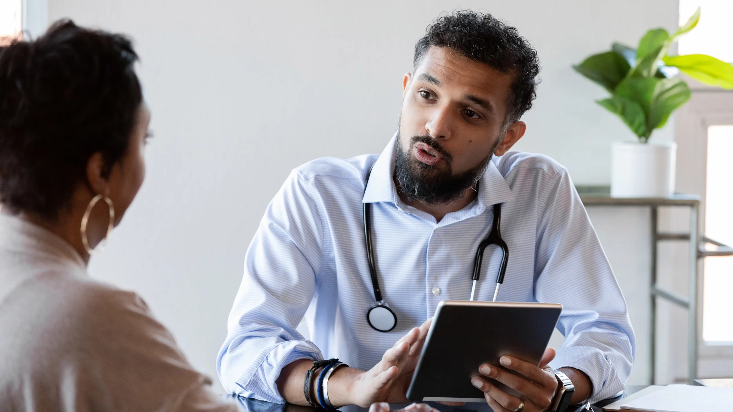 A doctor holding a tablet and talking to a patient.