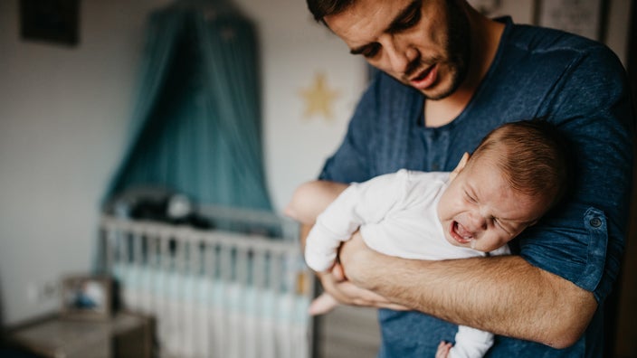 Man rocking baby to calm them from crying in the nursery room.