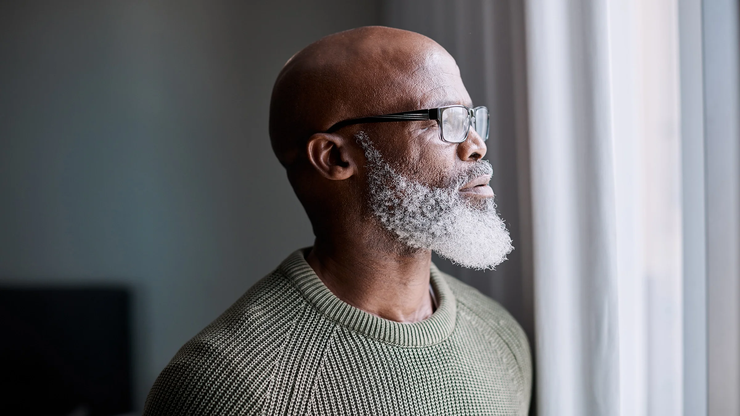 A man looks thoughtfully out a window at home.