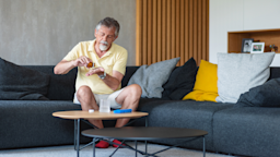 A man is sitting on his living room couch, taking medication from a pill bottle.
AzmanJaka/E+ via Getty Images