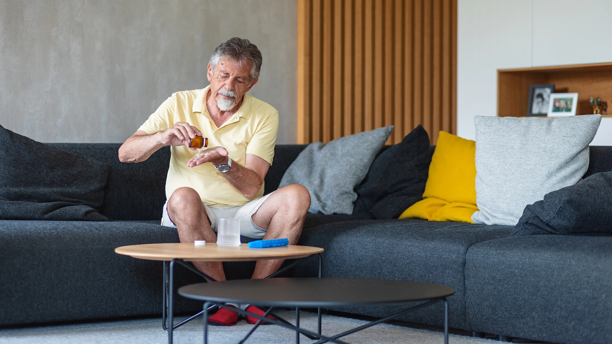 A man is sitting on his living room couch, taking medication from a pill bottle.