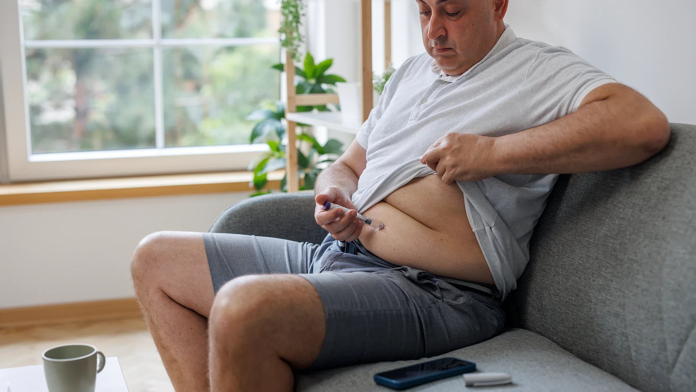 A man sitting on the sofa injects insulin in his abdomen.
Constantinis/E+ via Getty Images Plus          