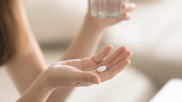 Cropped shot of a woman's hand holding a single white pill. In her other hand there is a glass of water.
fizkes/iStock via Getty Images