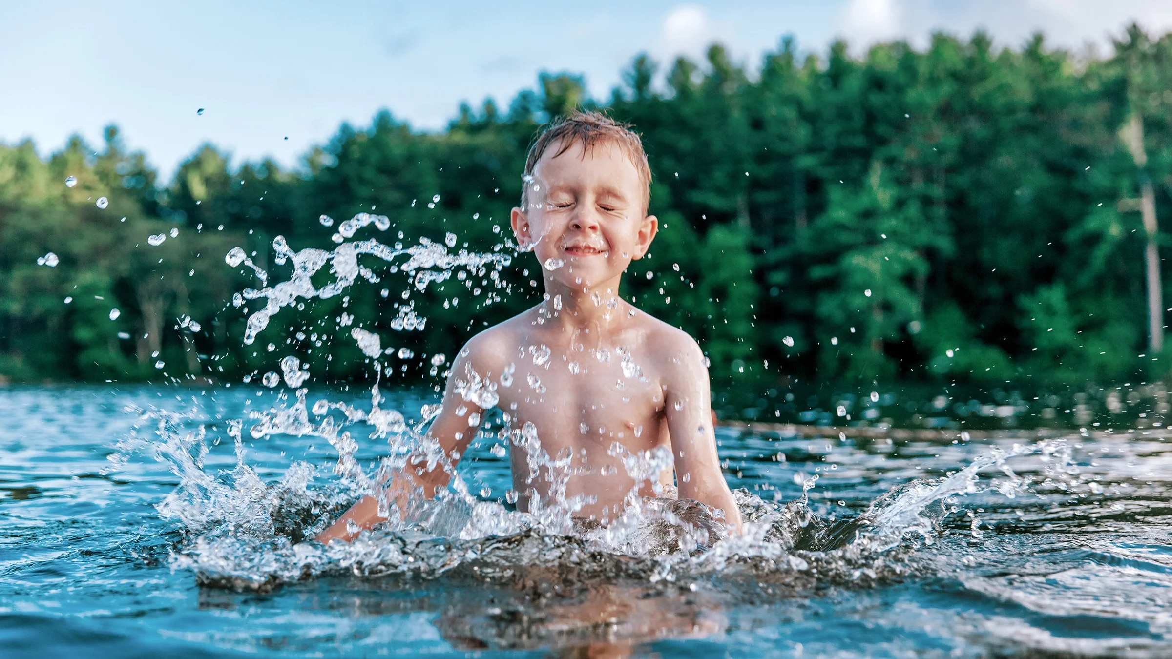 A young boy is swimming in a lake. He’s making big splashes and having fun.