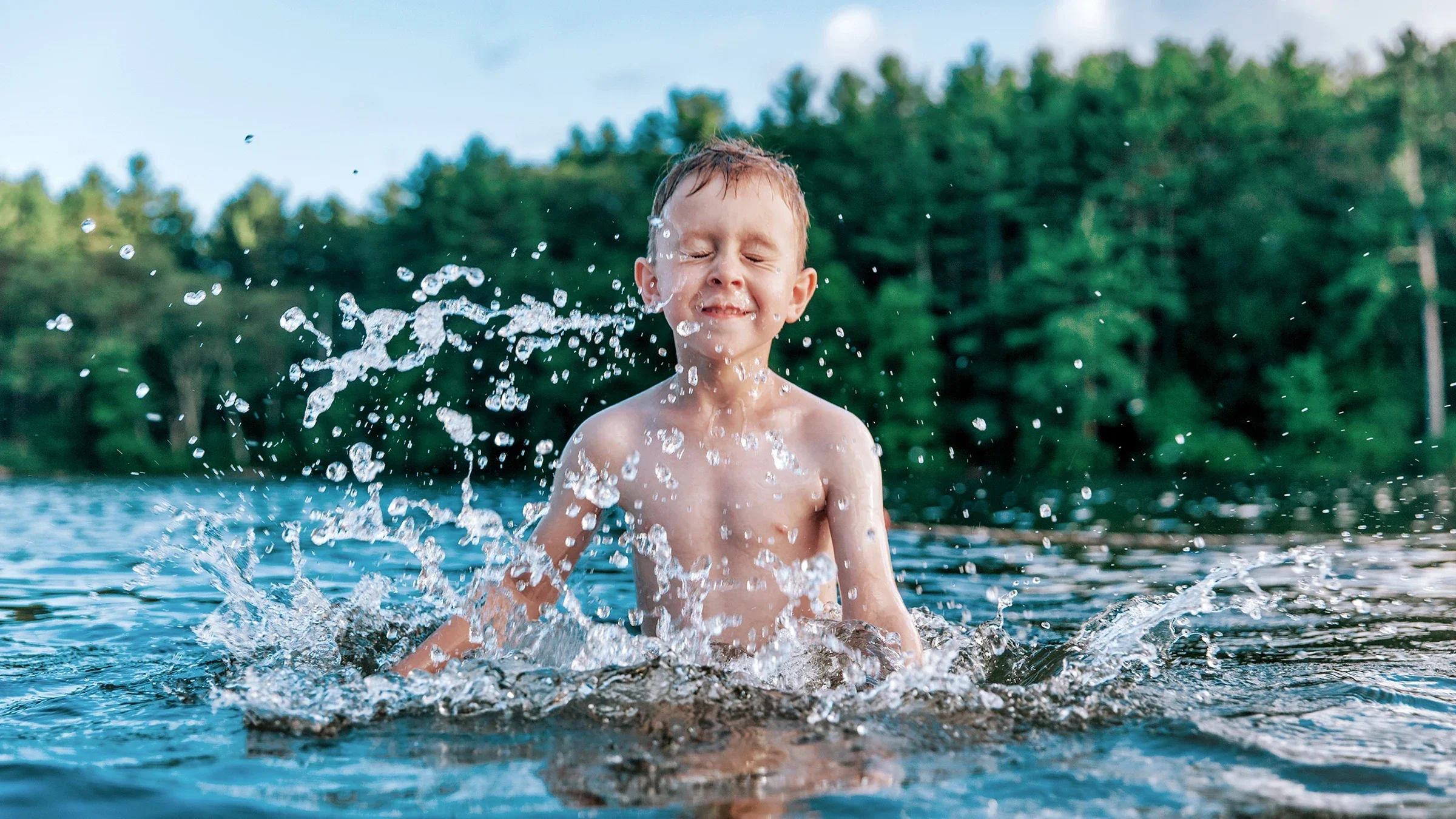 A young boy is swimming in a lake. He’s making big splashes and having fun.
EvgeniiAnd/iStock via Getty Images