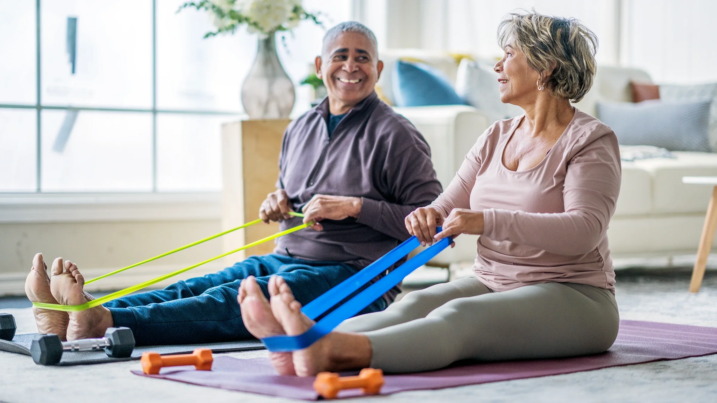 A couple exercise with resistance bands in their living room. 