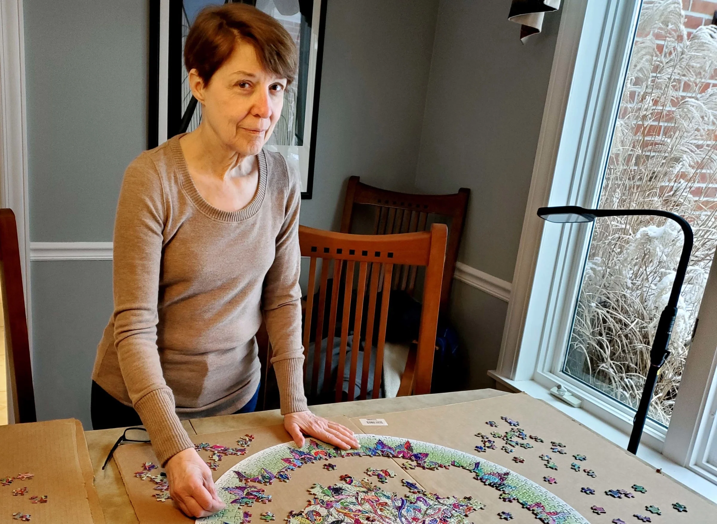 Woman standing over a table putting together a puzzle.