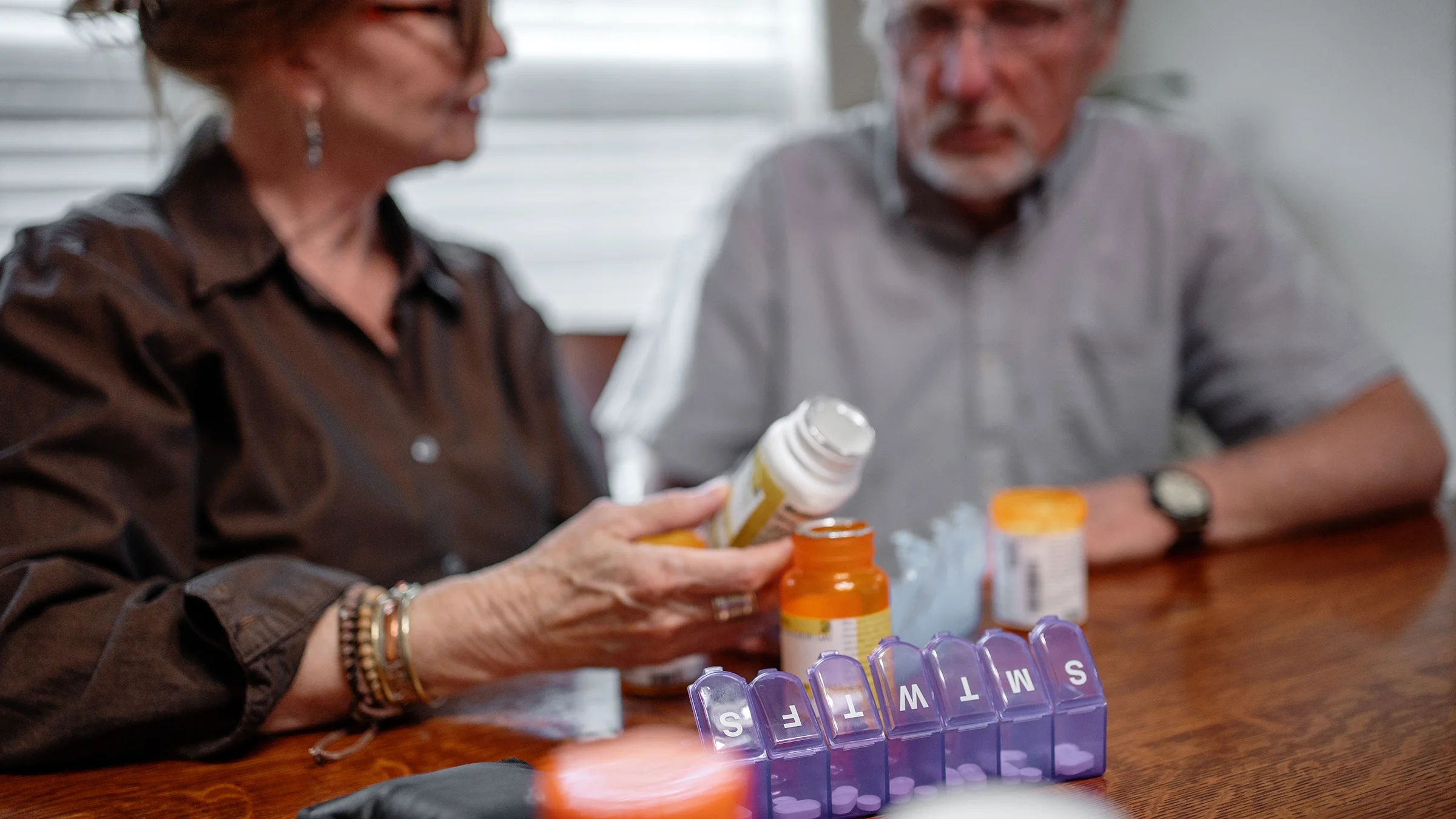 A couple places medication into a weekly pill organizer.
